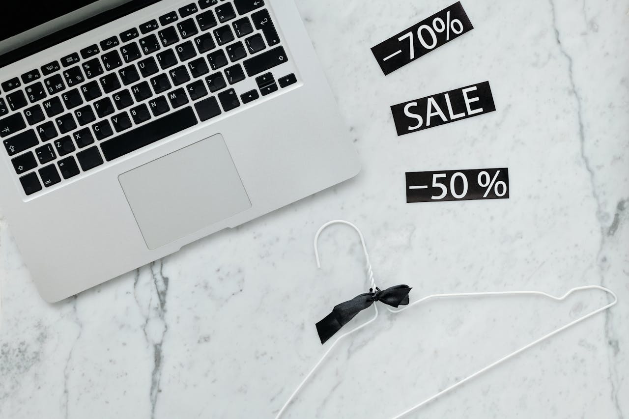 Flat lay of a laptop, hanger, and sale stickers on a marble desk, ideal for Black Friday themes.